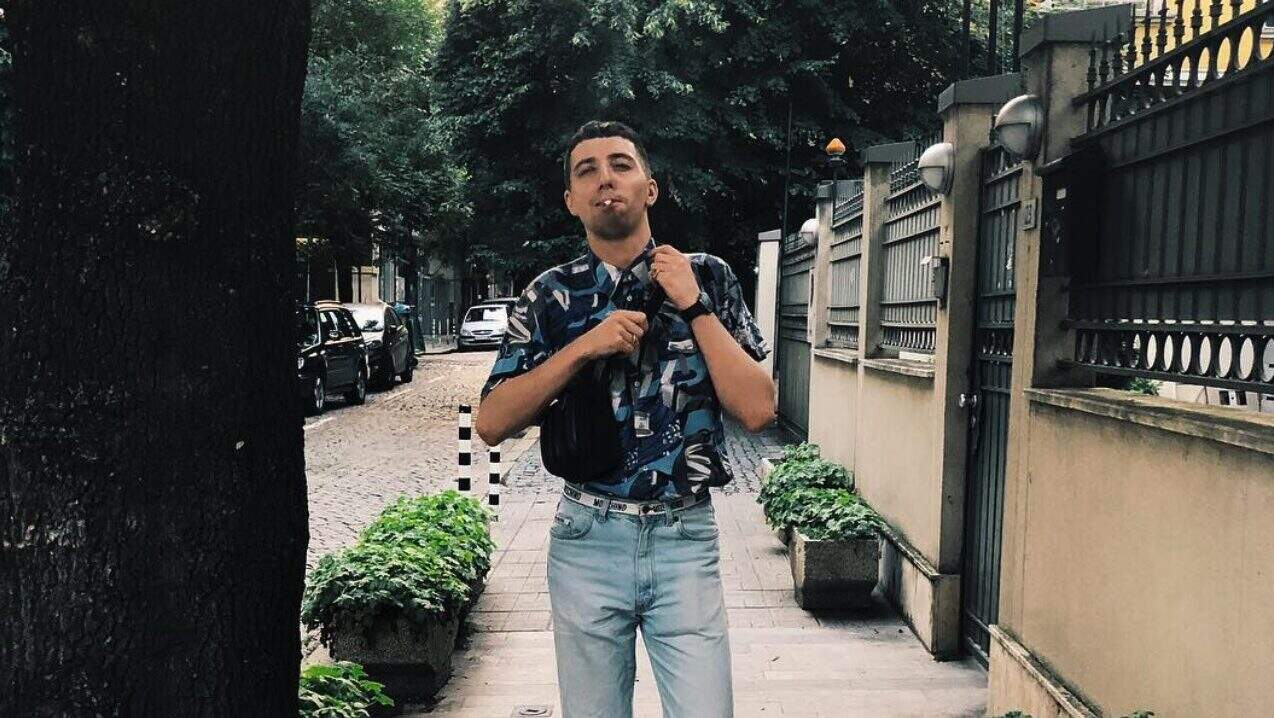 Wide urban street scene with young man carrying backpack, stylish casual clothing, and trees, in a neighbourhood setting for Lavery's, focusing on nightlife, bar, pub, and social gathering keywords.