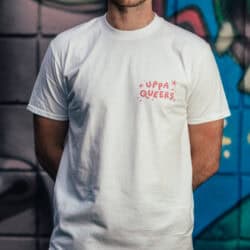 Bold white T-shirt featuring the playful "UPPA QUEERS" slogan in pink, stylishly worn by a young man against a colourful graffiti background, perfect for pride and LGBTQ+ apparel.