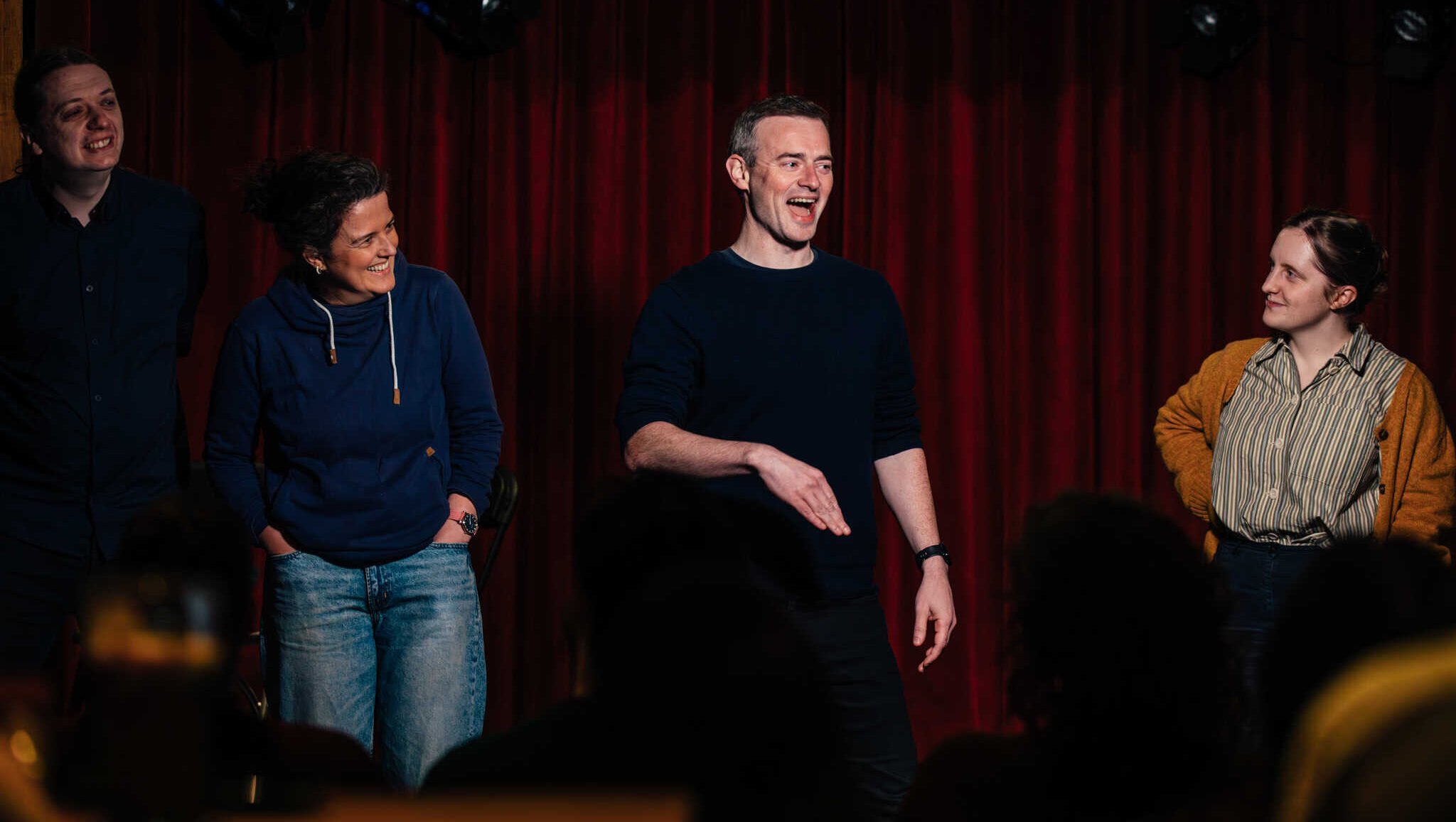 Lavery's comedy night with performers on stage laughing and engaging the audience in front of a red velvet curtain.