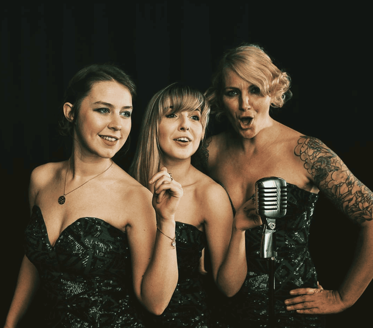 Three female singers performing live at Lavery's, with one holding a vintage microphone, during a concert by Claire McCartney & Charlie Hanlon.