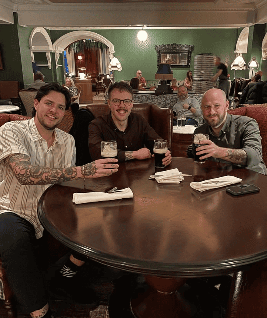 Three men enjoying drinks at Lavery's pub during a live music event, with a lively atmosphere and audience in the background.