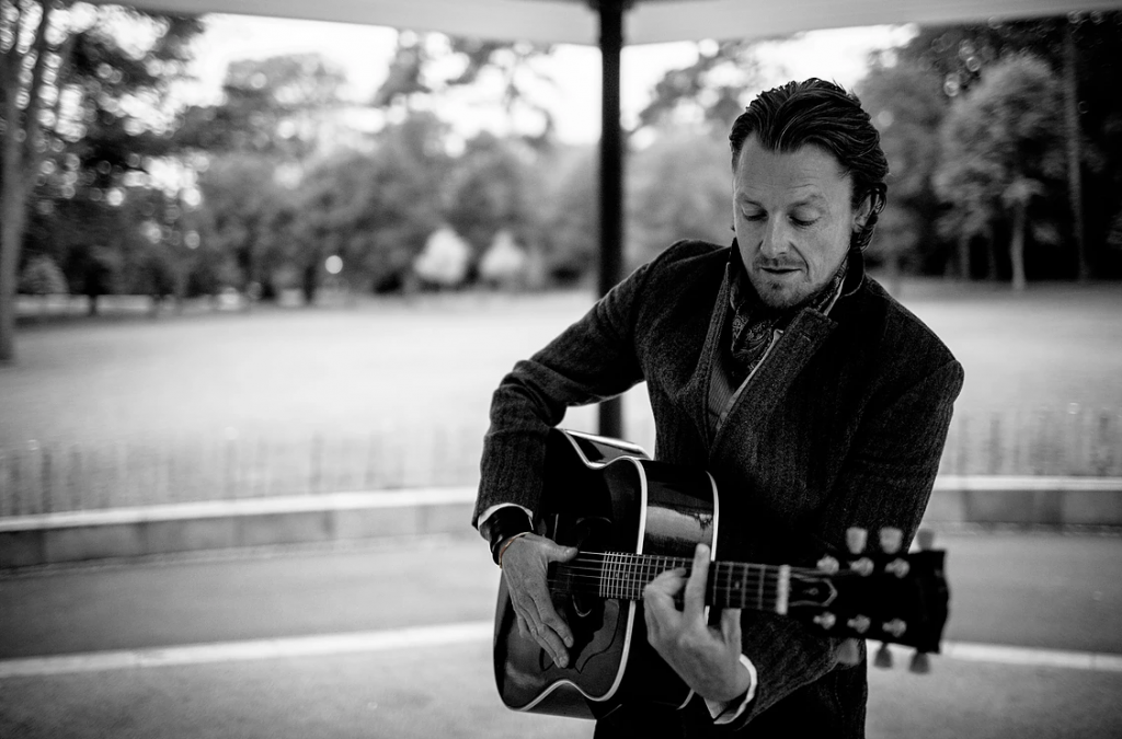 An image of Kyle John Suckling performing live at Lavery's, playing an acoustic guitar outdoors during a music event.