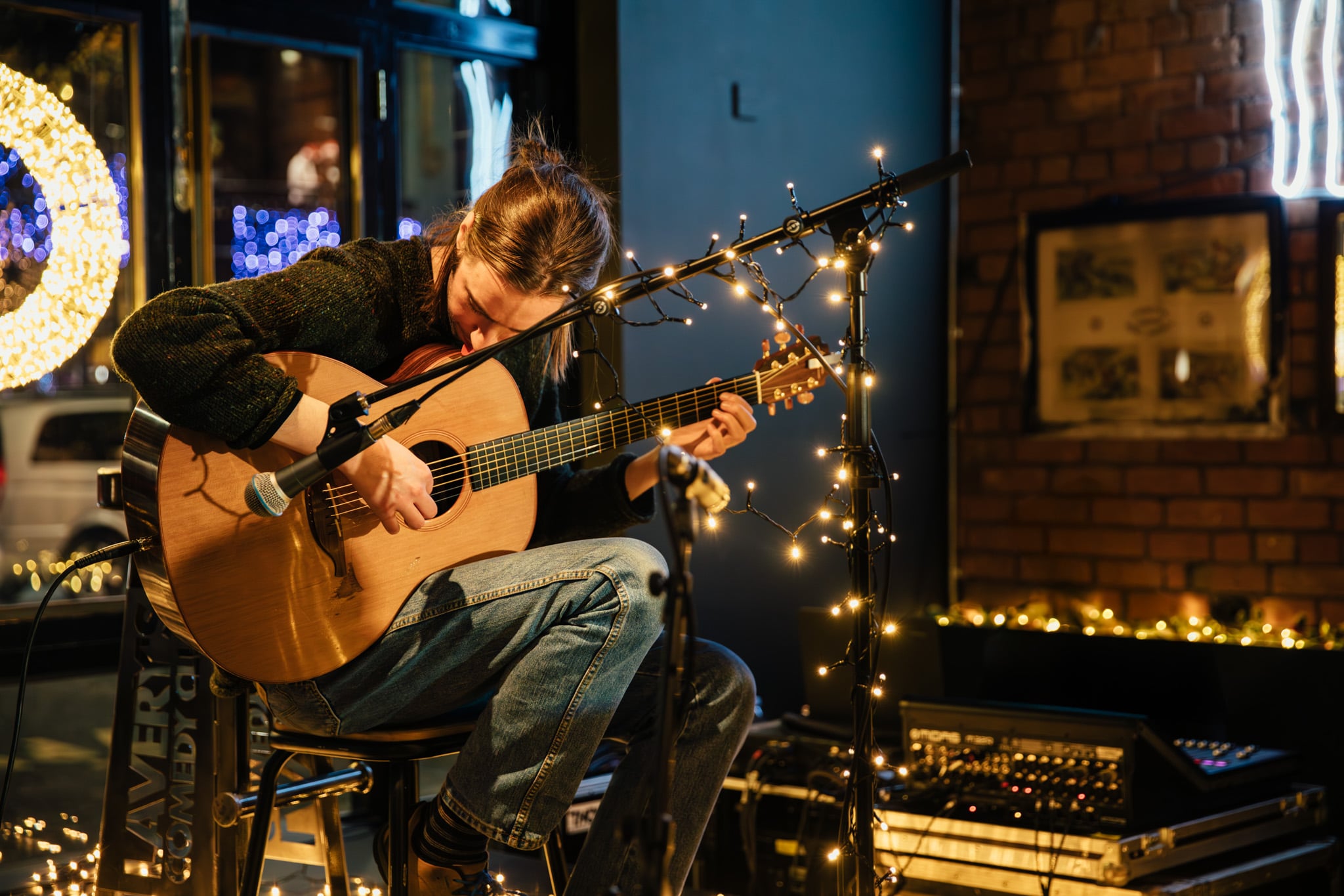 Young woman playing acoustic guitar during live music session at Lavery's, illuminated by warm string lights, in a cosy pub setting.