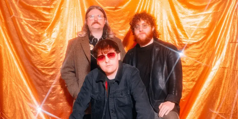 A band performing live on stage at Lavery's, with vibrant orange curtains in the background, showcasing energetic musicians in casual attire.