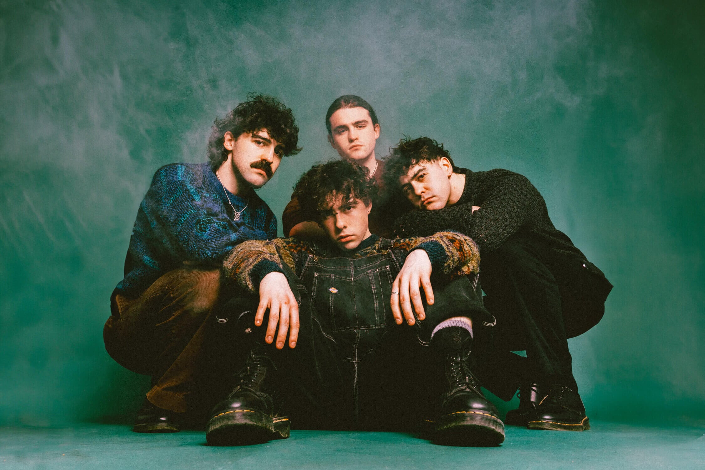 Stylish band portrait of Lavery's, a popular music group, featuring four members in trendy attire against a textured green background.